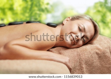 beauty, wellness and relaxation concept - close up of beautiful young woman having hot stone massage in spa over green natural background