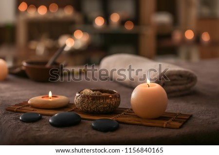 Burning candles, stones and towel on massage table in spa salon Royalty-Free Stock Photo #1156840165