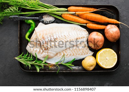 Cod. Fresh sea white raw fish before cooking in a with fresh vegetables: sweet onions, and lemons. Top view. Food concept