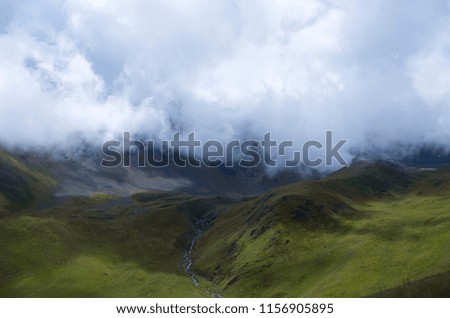 A colorful picture with a heavy fog on the top and bright green hills at the bottom. Nice mountain landscape in summer. 