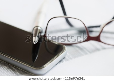 Cellphone pen and glasses on financial paper 