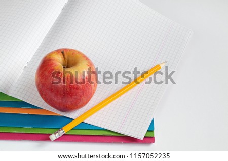 Pencil and apple on top of school notebook on white background. The theme of education