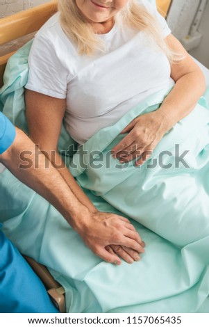 partial view of male nurse holding hand of sick senior woman lying in hospital bed 