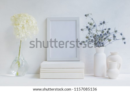 Home interior with decor elements. White frame, flowers in a vase, books