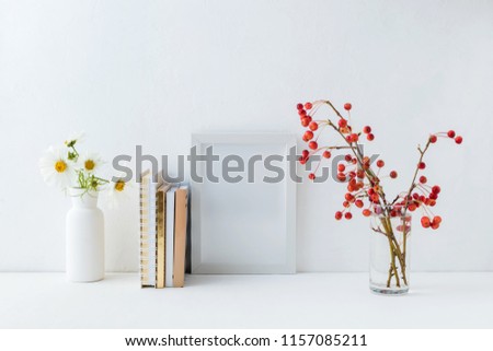 Home interior with decor elements. White frame, flowers in a vase, books