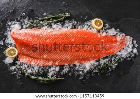 Fresh raw salmon fish steak with spices on ice over dark stone background. Creative layout made of fish, top view, flat lay Royalty-Free Stock Photo #1157113459