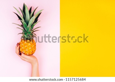 Hands with pineapple on stylish pink and yellow background.