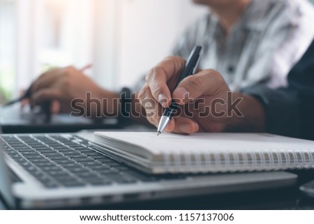  Elearning, online working concept. Business man working on laptop computer, searching and taking note on paper notebook with pen. Students attending course online class
