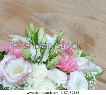 Blurred picture (soft focus) of D color emerald cut diamonds engagement ring on sweet and beautiful flowers bouquet with wooden background and copy space