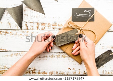 halloween concept. female hands with black nails wrapping a halloween gift on white wooden table top view