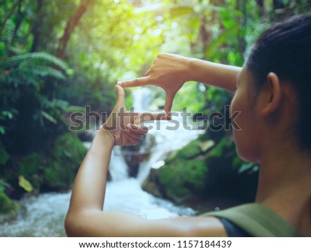 The woman making frame round the waterfall with her hands in the rain forest,copy space,warm retro tone.