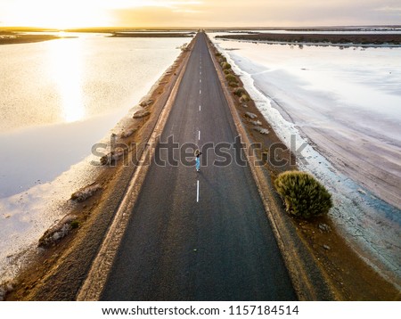 Girl standing in centre of long empty road during sunset. Lake King, Western Australia, Australia.