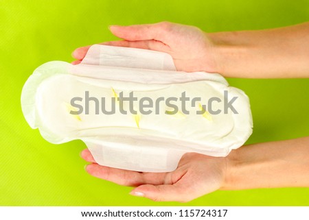 woman's hands holding a sanitary pad on green background close-up