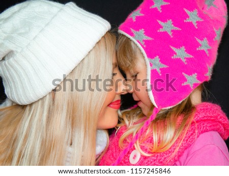 Mom and daughter embrace, in knitted hats, on a black background. Happy family, smiles and joy.