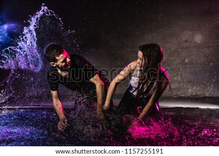 Couple young Teens together in small pool, drops of water and colored light behing them