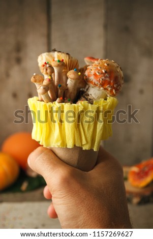fantastic ice cream with candy mashroom in hand on wooden background, concept of poisin, nagic food, halloween holiday funny food