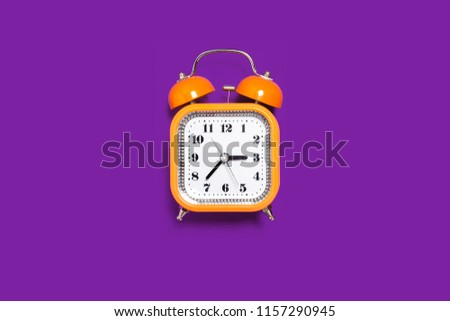 Vintage style orange metal alarm clock with bells standing on the purple surface isolated. back to school concept. free space for text Royalty-Free Stock Photo #1157290945