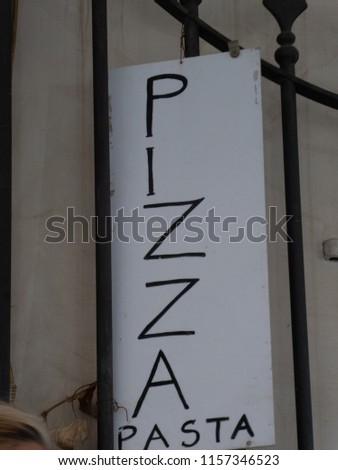 Vertical handwritten placard with the Italian text "Pizza Pasta" outside a door