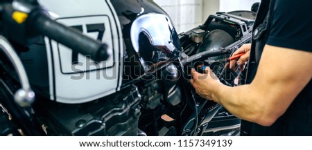 Mechanic repairing customized motorcycle by changing a fuse in the workshop