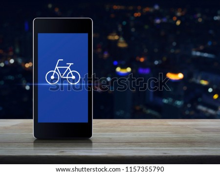 Bicycle flat icon on modern smart mobile phone screen on wooden table over blur colorful night light city tower and skyscraper, Business bike shop online concept