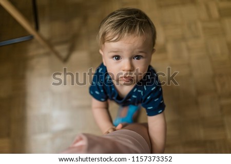 Portrait of a boy, embracing mother's leg and asking to talk. Baby with brown eyes holds onto mom leg while sweetly, longingly looking up at his parent. Family, child, childhood and parenthood concept