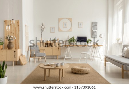 Wooden table and pouf on carpet in white living room interior with poster and workspace. Real photo