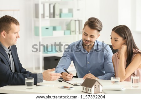 Young man signing a contract for buying house in office of estate agent