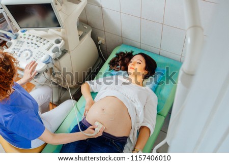 Top view of of ultrasound examination of the fetus. Red haired woman gynecologist testing pregnant woman in gynecological clinic. Prenatal testing.