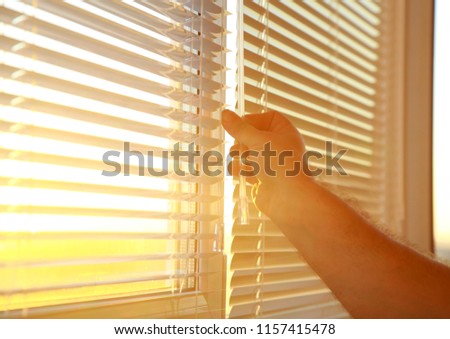 Man's hand opens the horizontal blinds on the Windows.