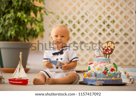 Little toddler boy, dressed as sailor, celebrating his first birthday with sea theme cake, boat, fishes and aqua animals, green backgground