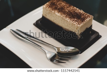 Cheese cake served on white plate together with silverware, ready to eat, on the dessert prinkle with cocoa powder