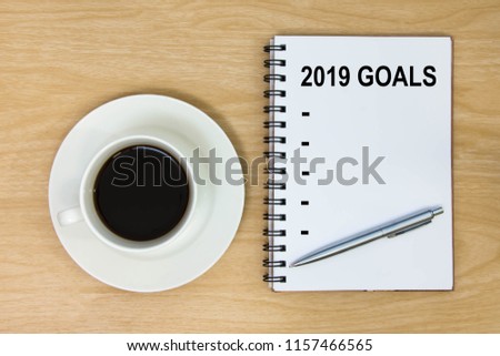 List year 2019 goals on paper wood table background.
New Year's Resolution on book and hot coffee cup.
Target success concept. 
top view.