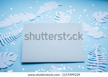 mockup card with tropical leaves. invitation card with environment and details Mockup with postcard and handmade paper leaves on blue background.