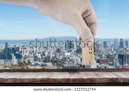 Hand choosing mini wood house model with blur building background.  Planning to buy property. Choose what's the best. A symbol for construction ,ecology, loan concepts