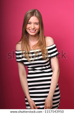 Beautiful toothy laughing blond long stright hairstyle woman in striped dress posing on pink background. 