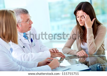 Portrait of two practitioners consulting patient with headache in hospital