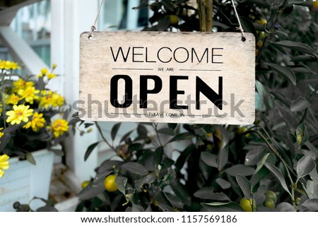 Welcome Open sign hanging by rope on rustic antique wood door on tree background
