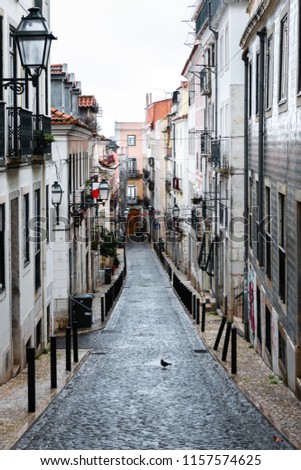 Traditional narrow cobblestone street in the Barrio alto district in Lisbon on a rainy Winter morning, with incidental people in the background.