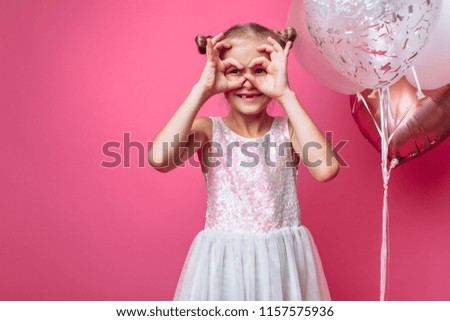 portrait of a little girl with balls, on a pink background in a photo Studio