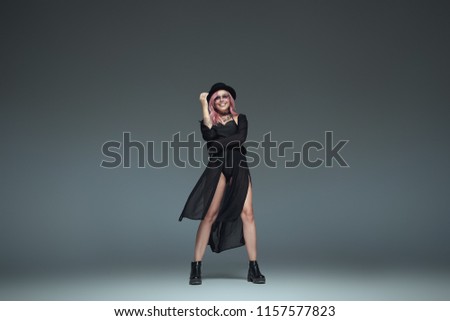 Two fashionable girls wearing black trendy outfits, accessories, sunglasses, hat and leather boots posing on studio gray background standing in fashion body pose.
