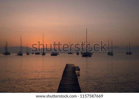 Scenic view of wooden pier and sailing boats at the calm sea on beautiful pink and orange sunset. Mountains on background. Twilight