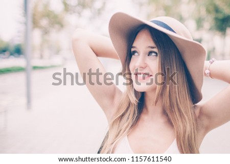 Closeup portrait of smiling young beautiful fair-haired woman keeping her arms behind head and standing outdoors in summer