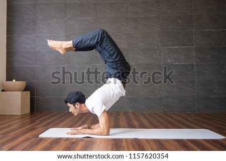 Experienced yogi doing scorpion yoga pose in gym. Man looking at camera and practicing yoga. Yogi concept. Side view. Royalty-Free Stock Photo #1157620354