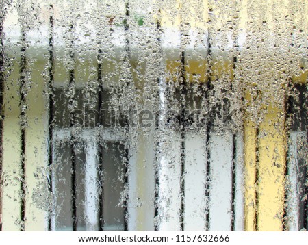 Glass texture background of water droplets condensation in the room and outside the window, the yellow building opposite background on a rainy day.
                               