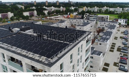 Aerial photo of modern apartment building roof filled with photovoltaic solar panels which absorb sunlight as source of energy to generate electricity also showing more living buildings in background
