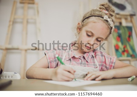 Blonde cute seven-year-old girl, draws at the table in the creative studio