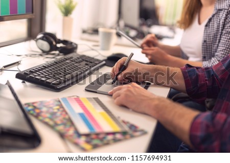 Designer working on a new project in an office; web designer drawing on a drawing pad and choosing colors from a color palette. Focus on the tip of the pen