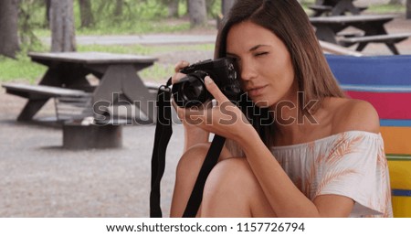 Attractive brunette taking photograph with camera sitting outdoors at campground