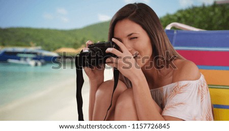 Millennial girl taking photo with camera while sitting at beach near some boats