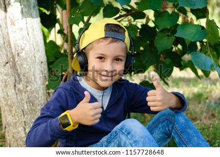 Young boy in headphones listening to modern music in nature. Child likes the song. Kid shows a thumbs up.